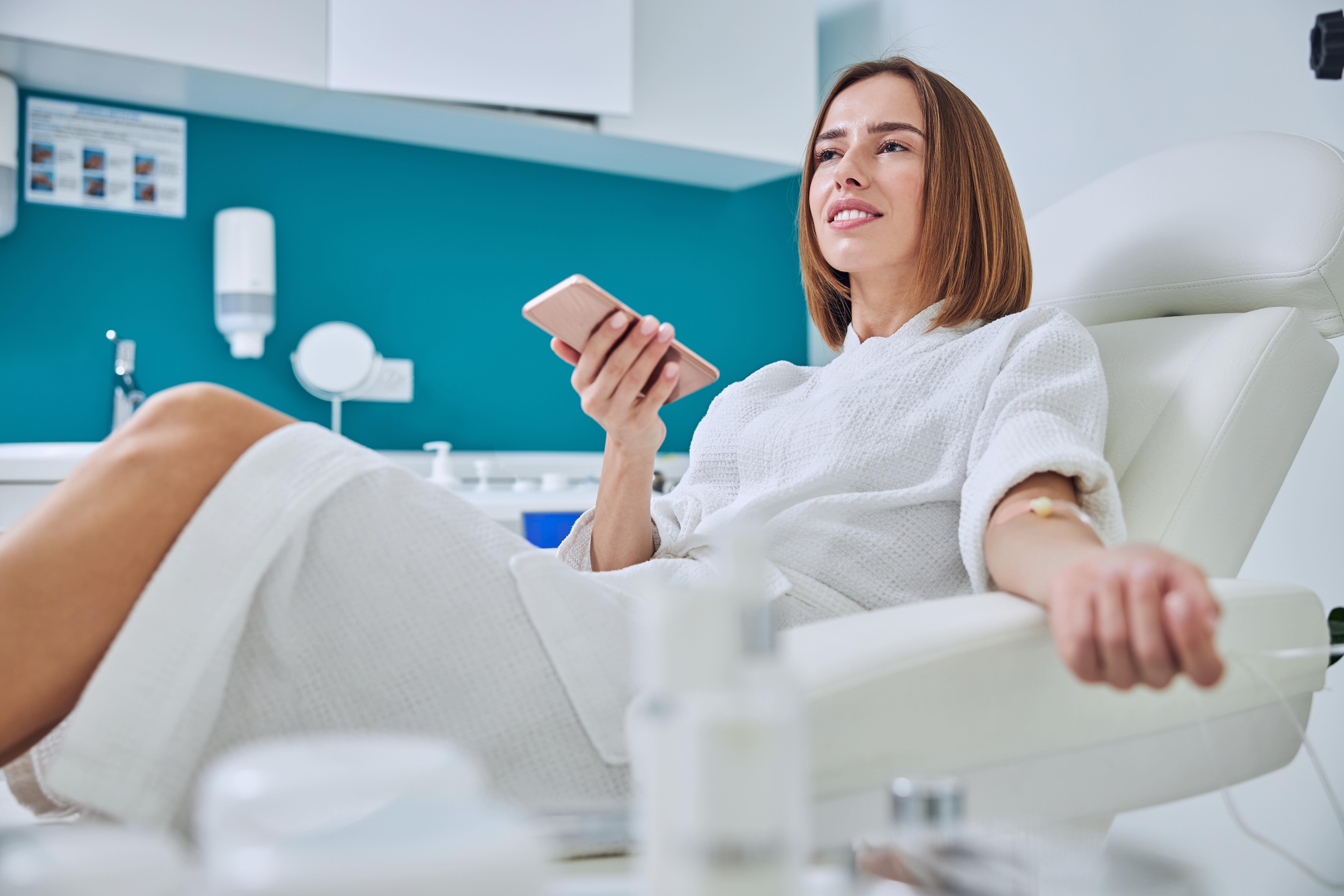 Woman relaxing in a clinical chair receiving IV treatment while holding her phone